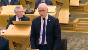 This photo appears to be Scottish Deputy First Minister and acting Finance Minister, John Swinney, delivering his budget to the Scottish Parliament. The budget included a 10 percent reduction in arts funding.